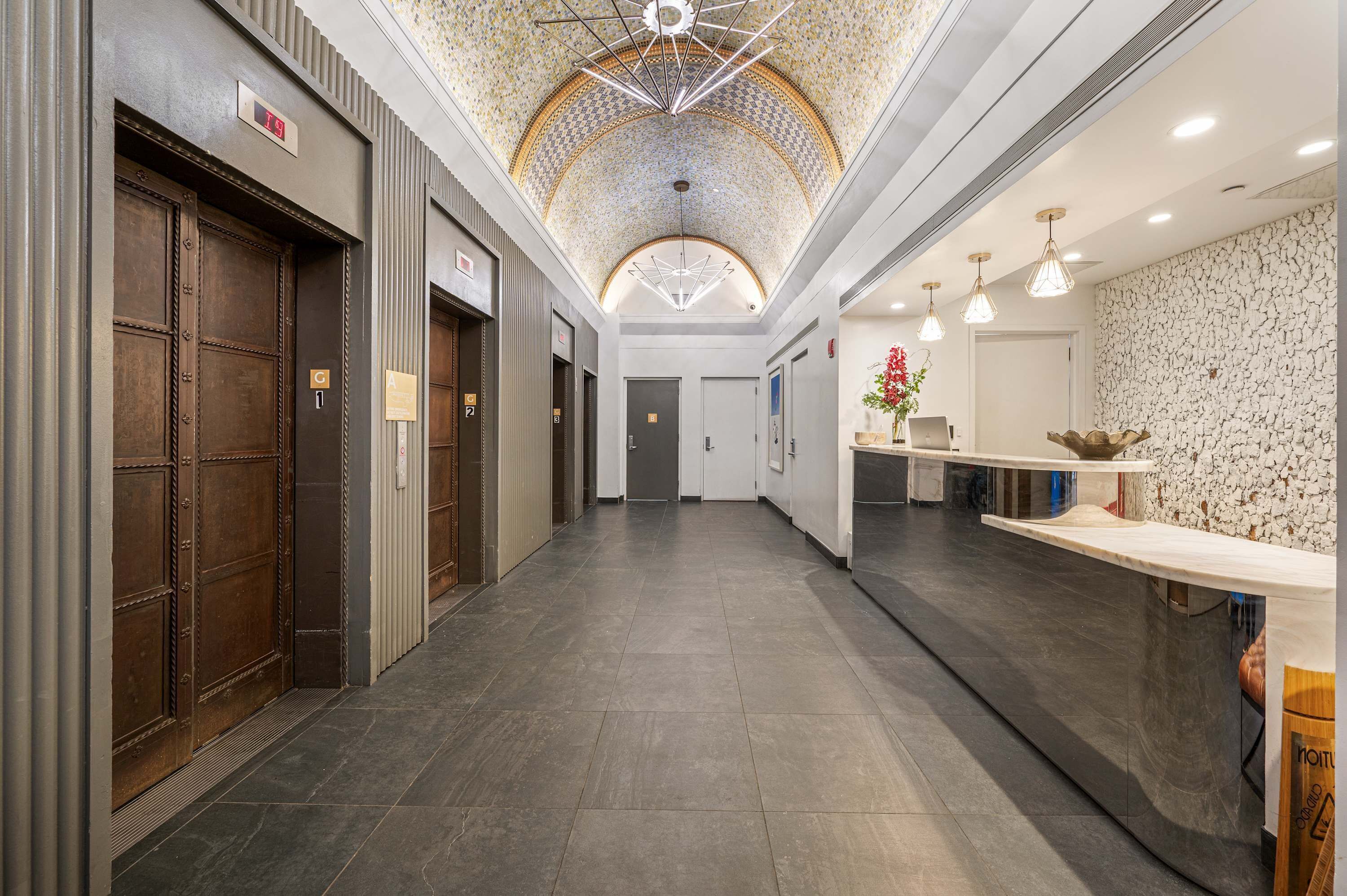 A hotel lobby with a tiled floor, a reception desk, and a ceiling with a geometric light fixture.