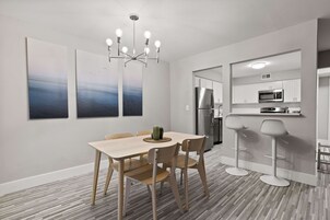 A modern kitchen with white cabinets, stainless steel appliances, and a bar area with stools.