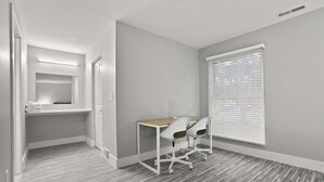 Une chambre moderne équipée d’un bureau et de deux chaises, d’une fenêtre avec des stores et d’un miroir au-dessus de la porte.