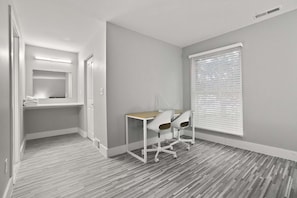 A modern room with a desk and two chairs, a window with blinds, and a mirror above the door. - Welcoming 2BR 2BA Retreat With Modern Comforts (Rochester)
