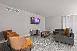 Una sala de estar moderna con un sofá gris, sillas naranjas, una mesa de centro de madera y un televisor de pantalla plana montado en la pared.