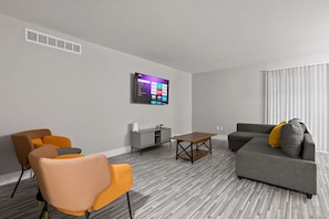A modern living room with a grey sofa, orange chairs, a wooden coffee table, and a flat-screen TV mounted on the wall. - Welcoming 2BR 2BA Retreat With Modern Comforts (Rochester)