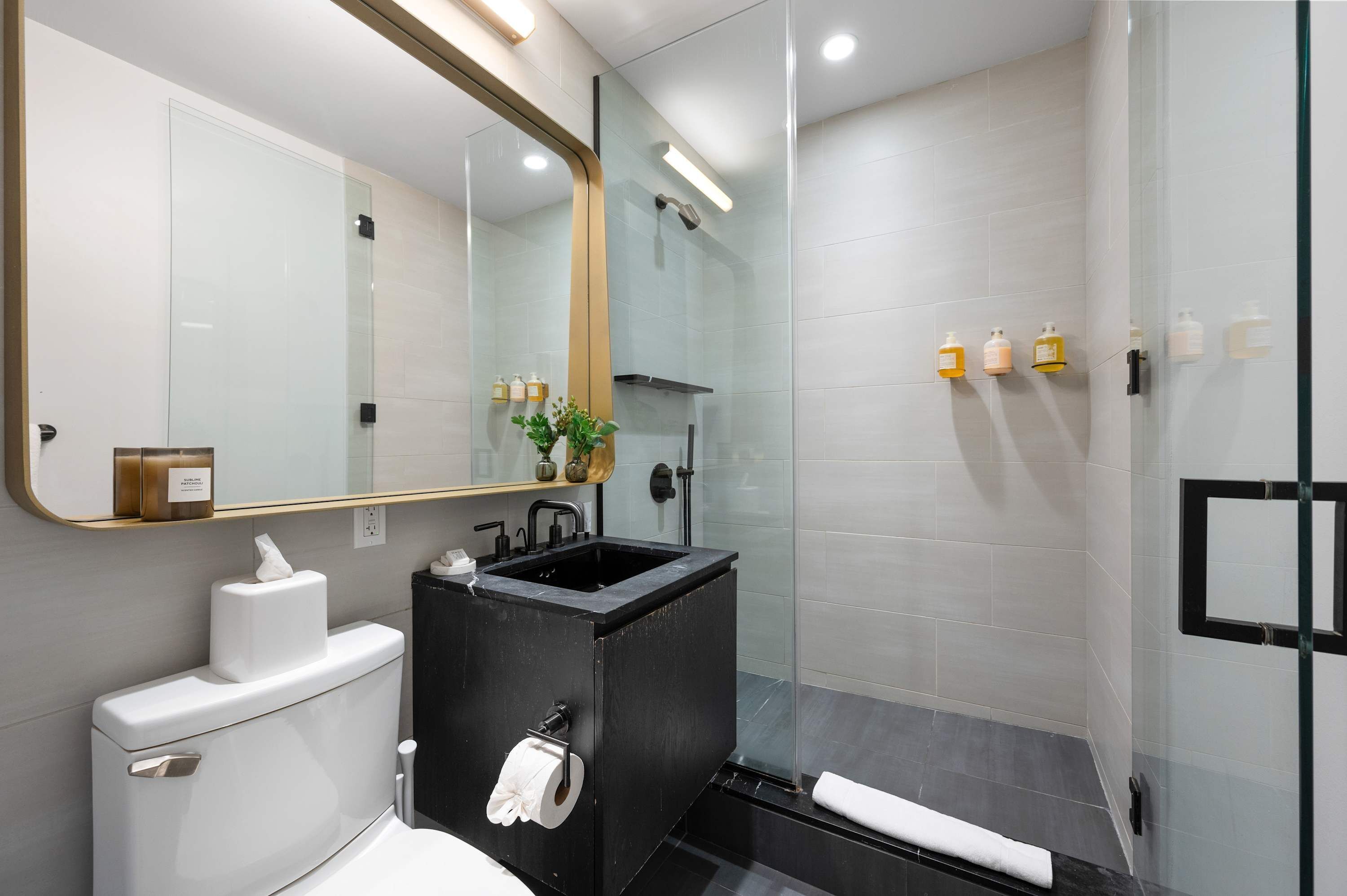 A modern bathroom with a glass-enclosed shower, a black sink, and a white toilet.