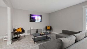Un salon moderne avec un téléviseur à écran plat fixé au mur, un canapé gris, une table basse noire et un autre canapé gris agrémenté d  ’un coussin jaune.
