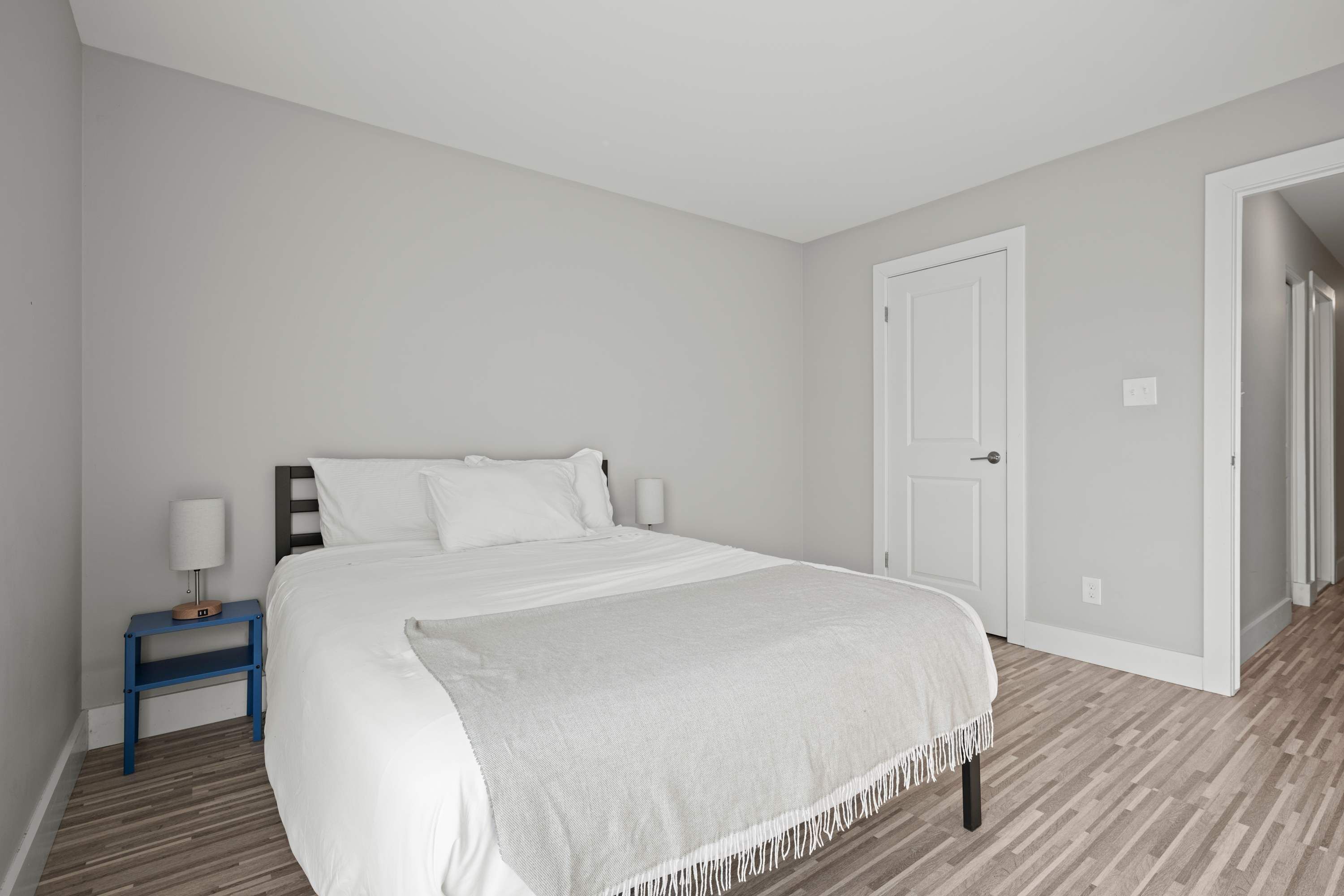 A bedroom with a bed, a nightstand, a door, and a hallway.