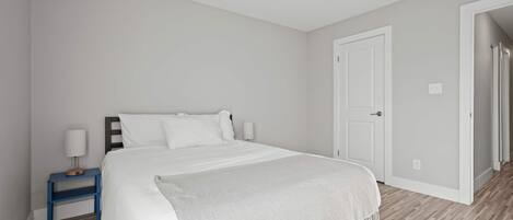 A bedroom with a bed, a nightstand, a door, and a hallway.