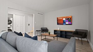 Ein modernes Wohnzimmer mit grauem Sofa, einem Couchtisch und einem an der Wand montierten Fernseher, der Streaming-Dienste anzeigt.