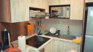 Une cuisine moderne avec des meubles en bois, un four à micro-ondes encastré, un évier en acier inoxydable et une plaque de cuisson noire.