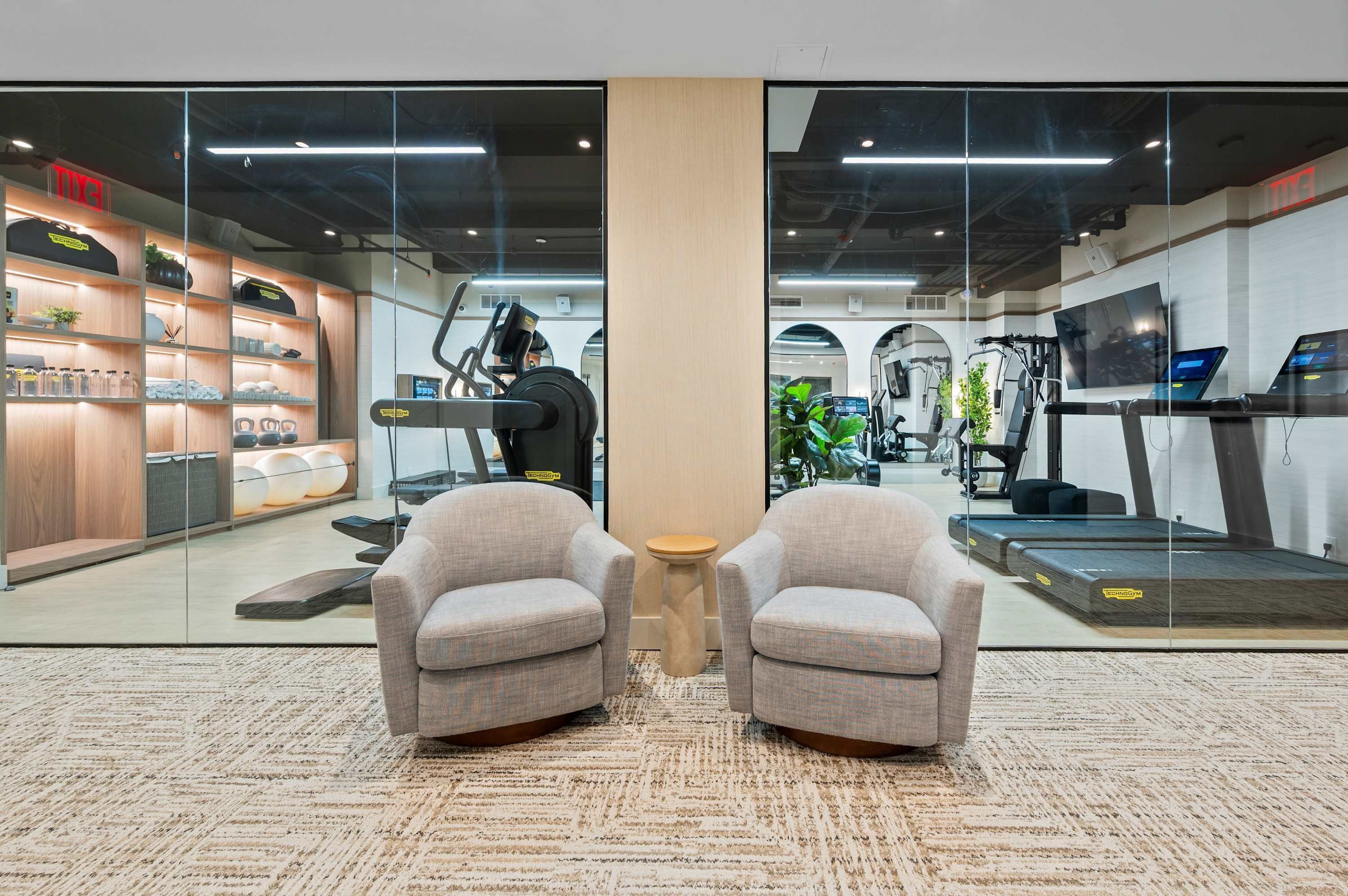 A gym with exercise equipment, a treadmill, and a pair of armchairs.