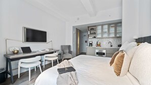 Ein modernes Hotelzimmer mit Bett, Schreibtisch mit Laptop, Stuhl, Fernseher und Küchenzeile.
