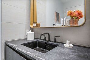 A bathroom with a black sink, a mirror, and a vase with flowers. - 17john: Queen Studio Apartment - Disability Access (New York)