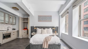 A modern bedroom with a large bed, a built-in wardrobe, a vanity with a mirror, and a window with a city view.