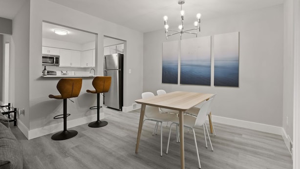 A modern kitchen with white cabinets, a microwave, and a refrigerator. There is a dining area with a wooden table and white chairs. - Cozy 2BR 2BA Apartment for the Family (Rochester)