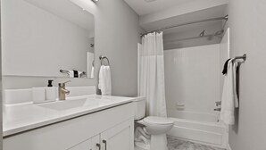 A modern bathroom with a white sink, mirror, and toilet. It includes a shower area with a glass door and a bathtub. - Cozy 2BR 2BA Apartment for the Family (Rochester)