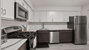 A modern kitchen with white cabinets, stainless steel appliances, and a black countertop. - Cozy 2BR 2BA Apartment for the Family (Rochester)