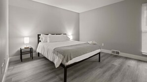 A bedroom with a bed, bedside table, lamp, and a window with blinds. - Cozy 2BR 2BA Apartment for the Family (Rochester)