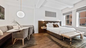 A modern bedroom with a bed, bench, bedside table, and a seating area with a table and chairs.