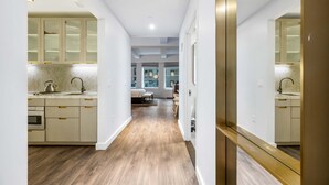 A modern kitchen with wooden flooring, white cabinets, and a dining area with a table and chairs. - 17john: Grand King Studio Apartment (New York)