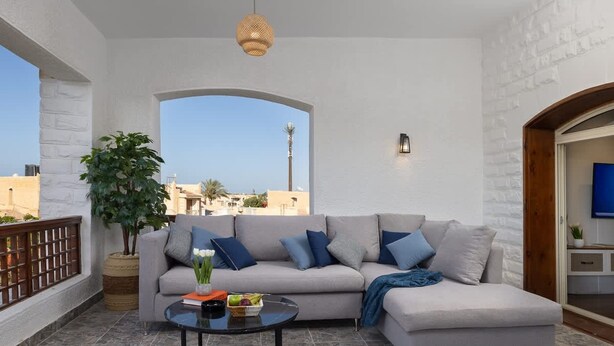 A balcony with a grey sofa, a round table, and a potted plant.