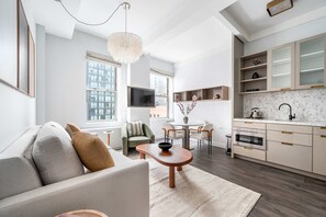 A modern living room with a sofa, a coffee table, and a TV. There is a dining area with a table and chairs, and a kitchen with cabinets and a sink. - 17john: Luxury One Bedroom Apartment (New York)