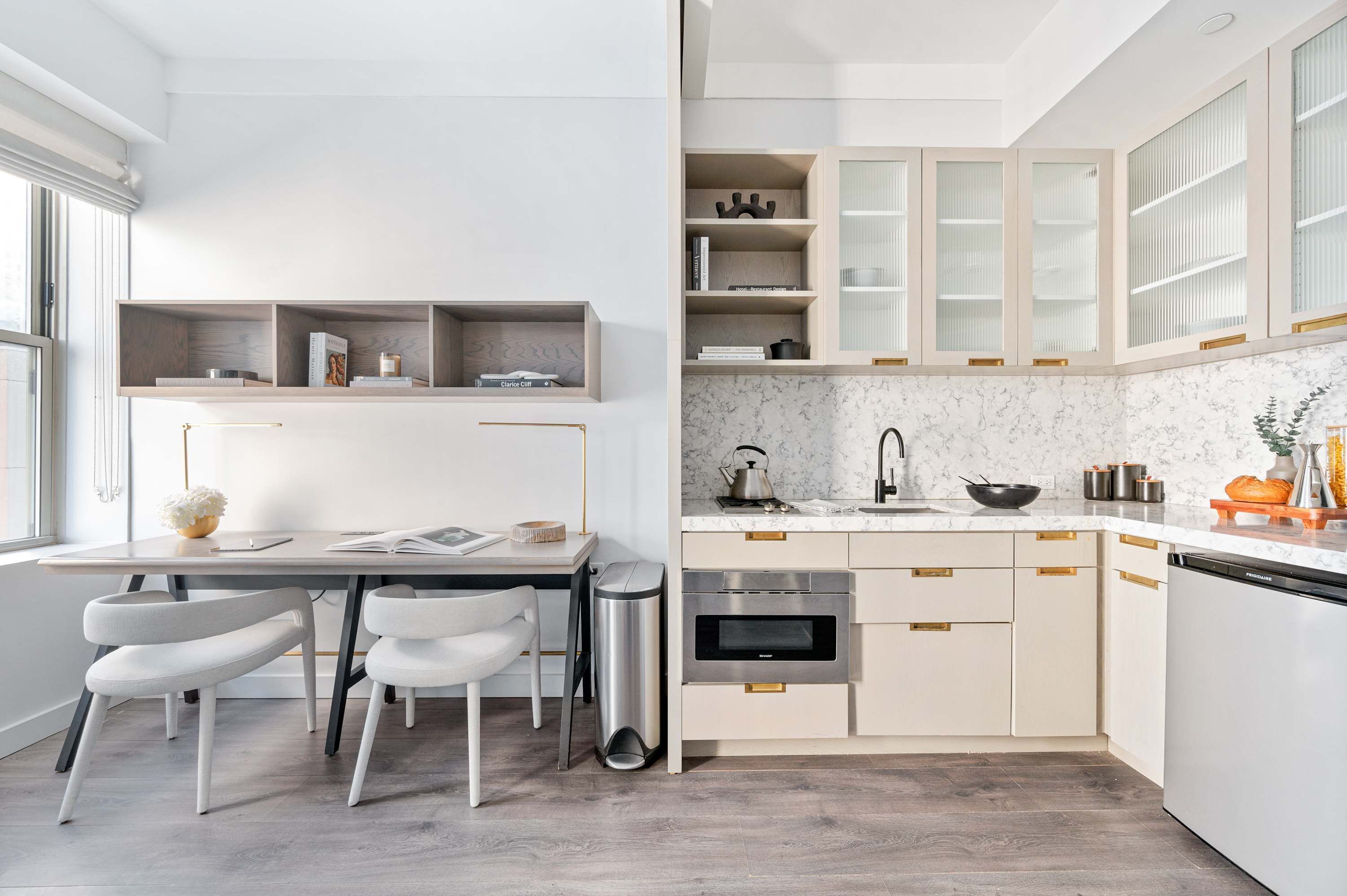 Een moderne keuken met inbouwapparatuur, een eethoek met witte stoelen en een raam dat natuurlijk licht binnenlaat.