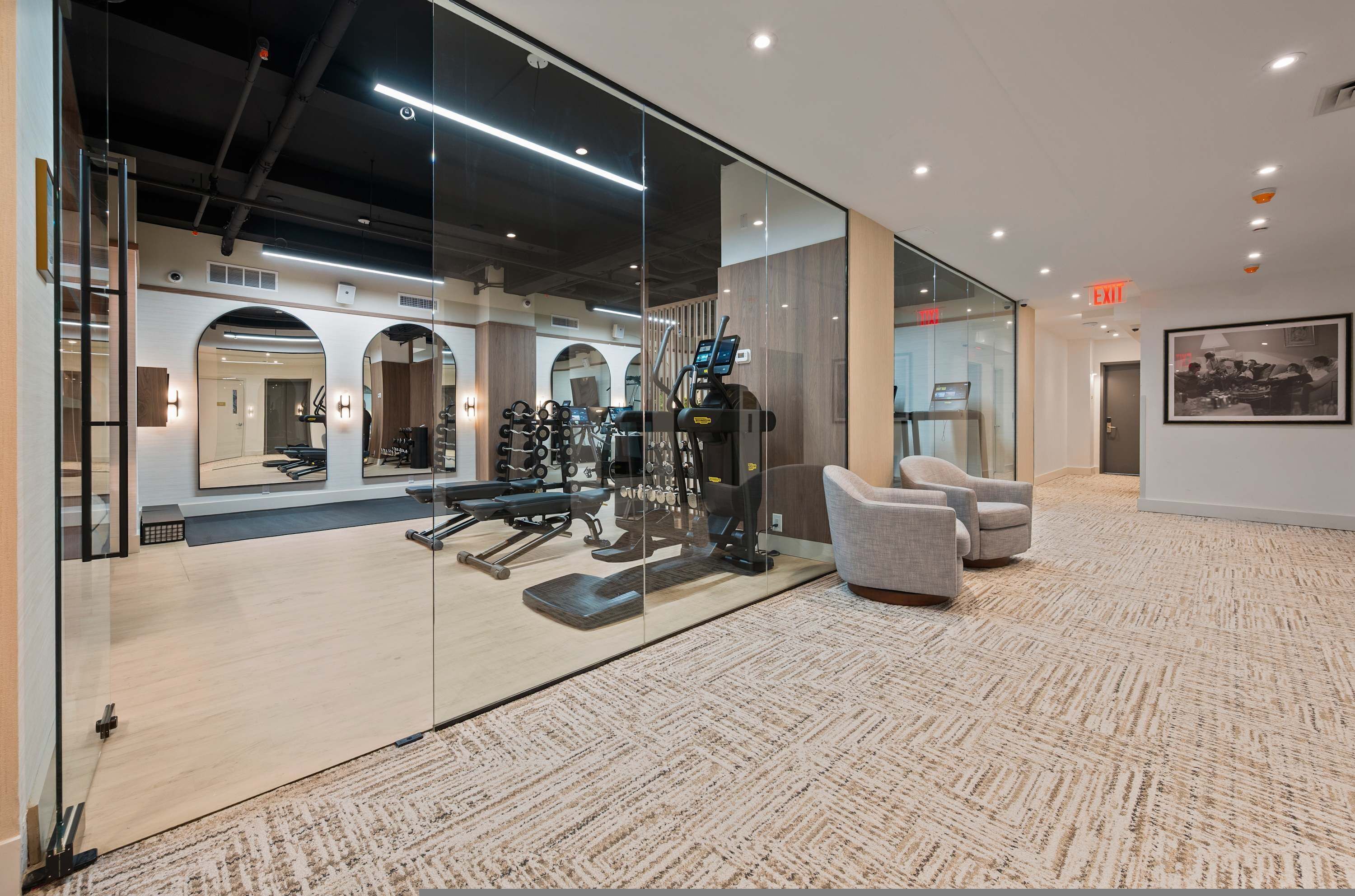 A modern gym with exercise equipment, a mirrored wall, and a carpeted floor.