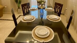 A dining room with a black table set for four, surrounded by chairs, a chandelier, and a potted plant. - Family Friendly Villa New Cairo (New Cairo)