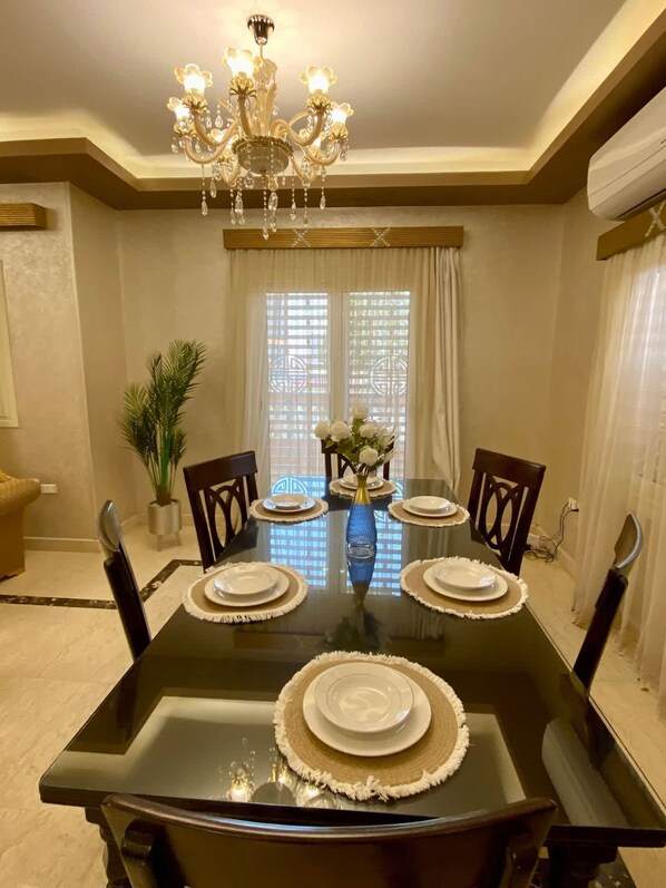 A dining room with a black table set for four, surrounded by chairs, a chandelier, and a potted plant. - Family Friendly Villa New Cairo (New Cairo)