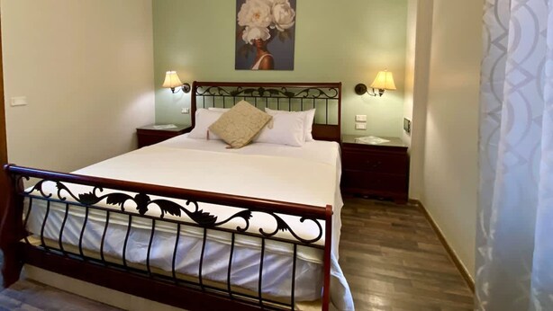 A neatly made bed with a headboard, two bedside lamps, a painting of flowers on the wall, and a patterned curtain. - Family Friendly Villa New Cairo (New Cairo)