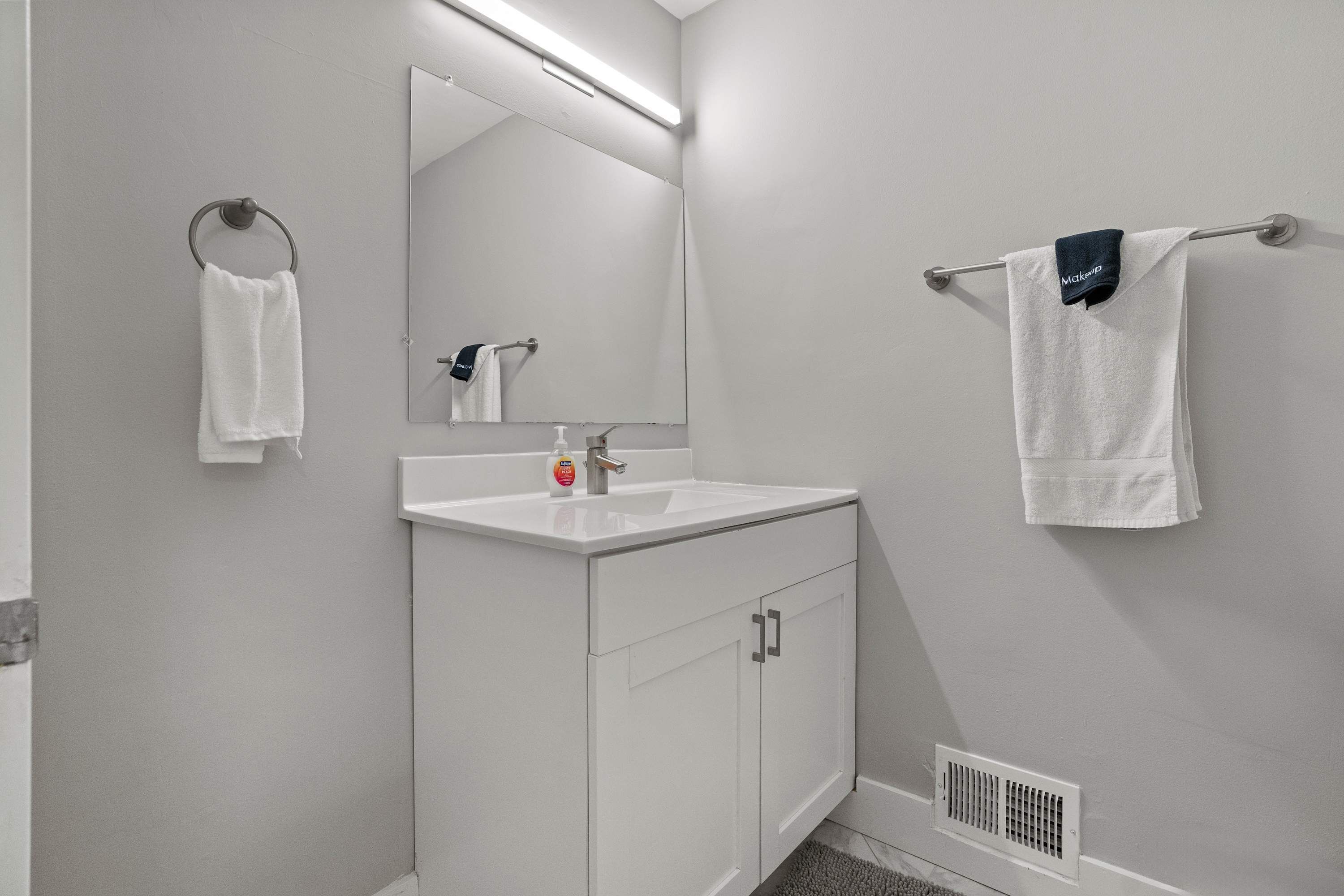 A bathroom with a white sink, a mirror, and two towels hanging on towel bars.
