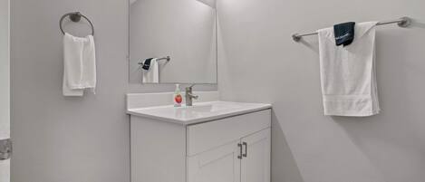 A bathroom with a white sink, a mirror, and two towels hanging on towel bars.