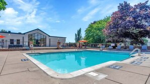 A swimming pool with lounge chairs and umbrellas, a building with large windows, and a tree with purple foliage. - Inviting 2BR 2BA Unit in Rochester Hills (Rochester)