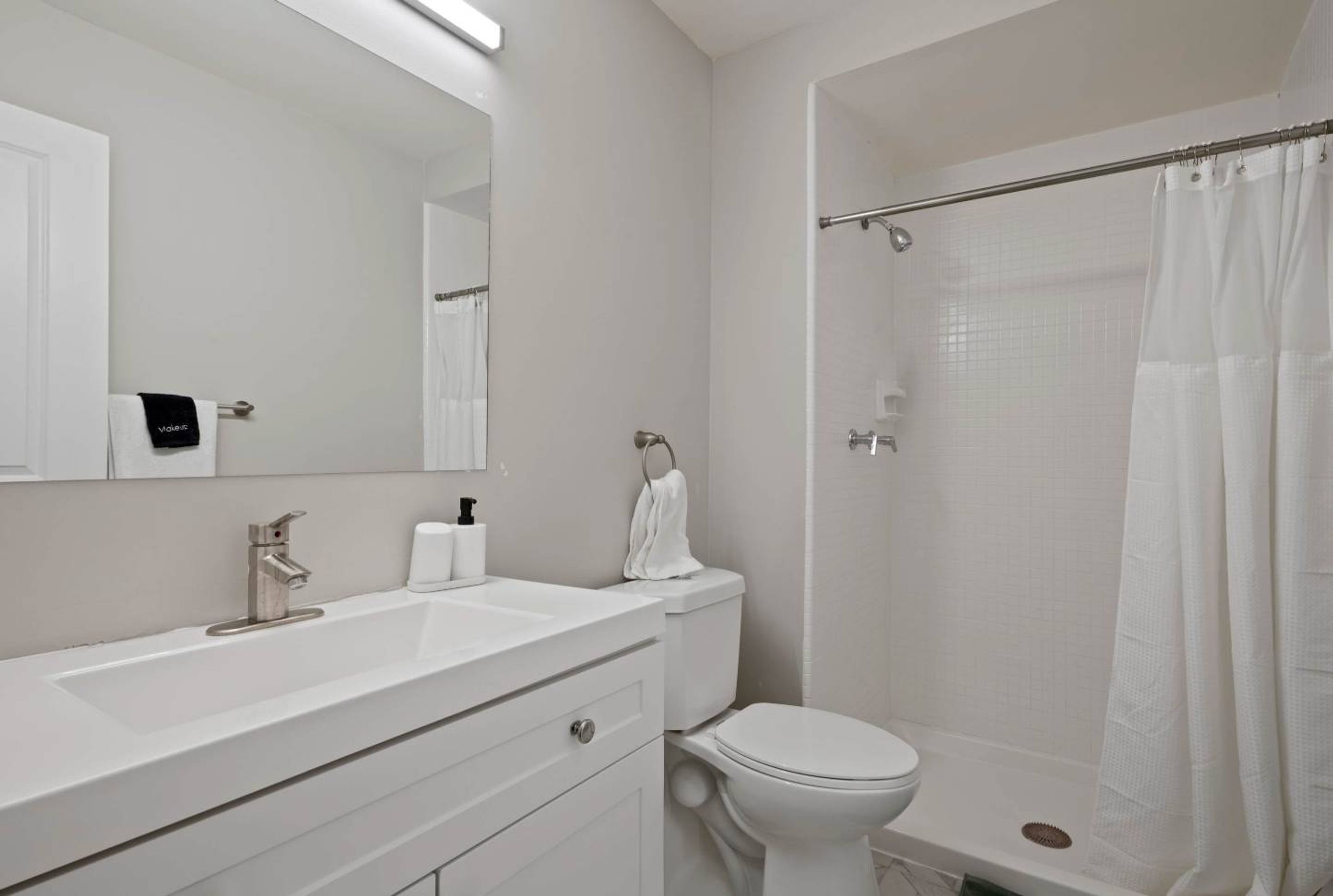 A modern bathroom with a white sink, mirror, toilet, and shower curtain.