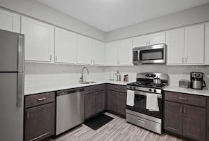 A modern kitchen with white cabinets, stainless steel appliances, and a black countertop. - Inviting 2BR 2BA Unit in Rochester Hills (Rochester)