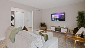 A modern living room with a sofa, coffee table, TV, and a plant. - Inviting 2BR 2BA Unit in Rochester Hills (Rochester)
