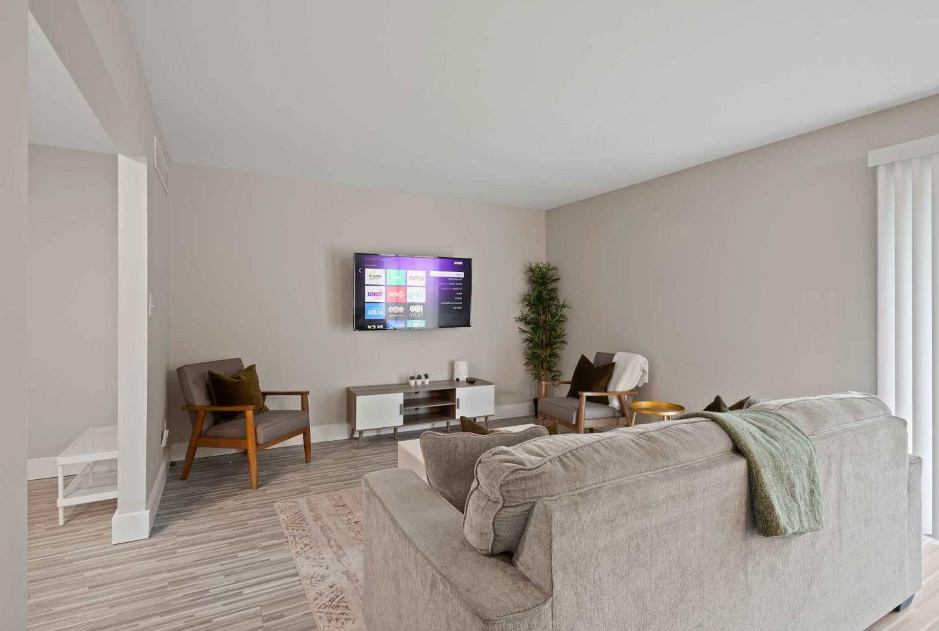 A modern living room with a grey sofa, a white entertainment unit, a TV mounted on the wall, and a small plant.