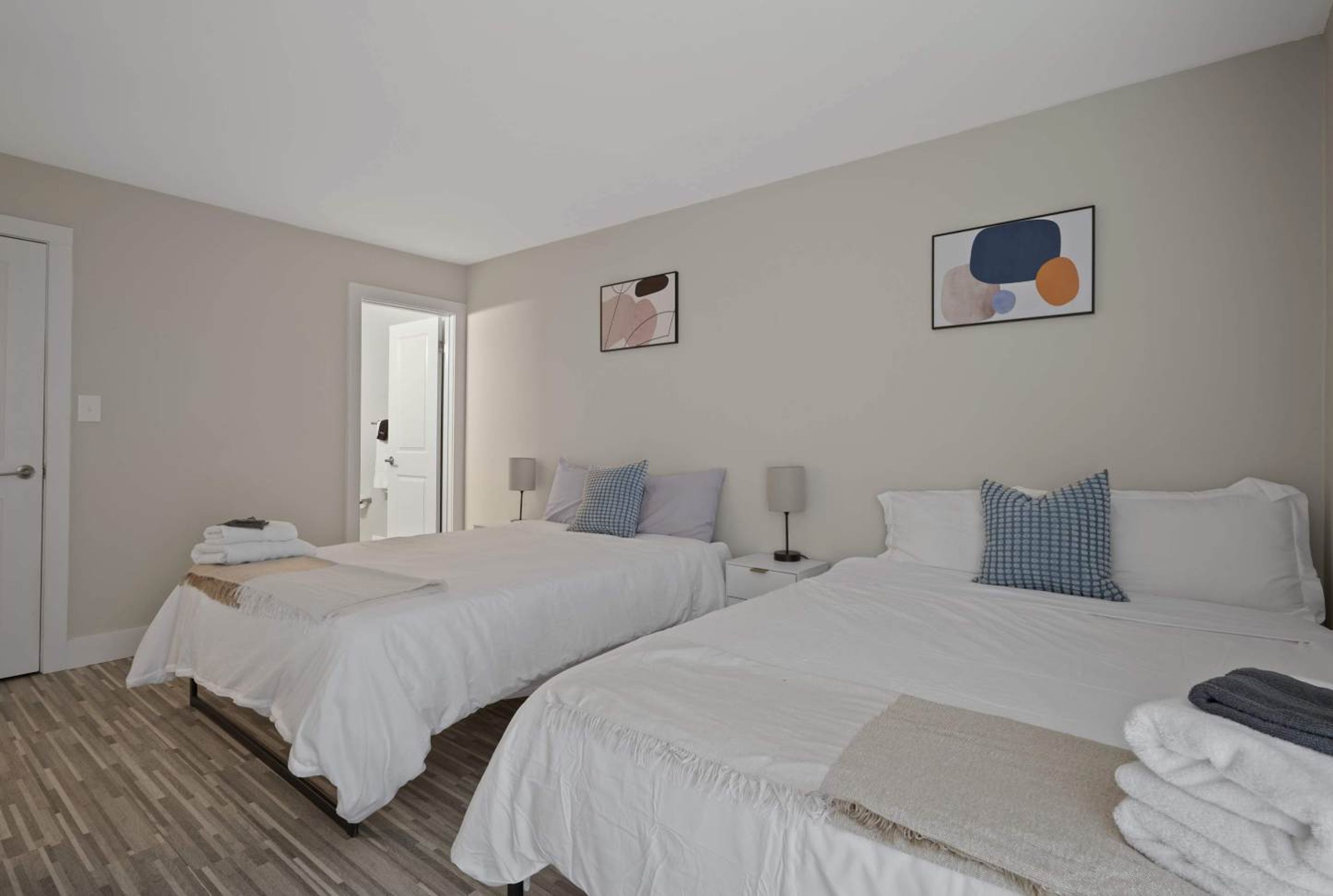 A hotel room with two beds, a door, and artwork on the walls.