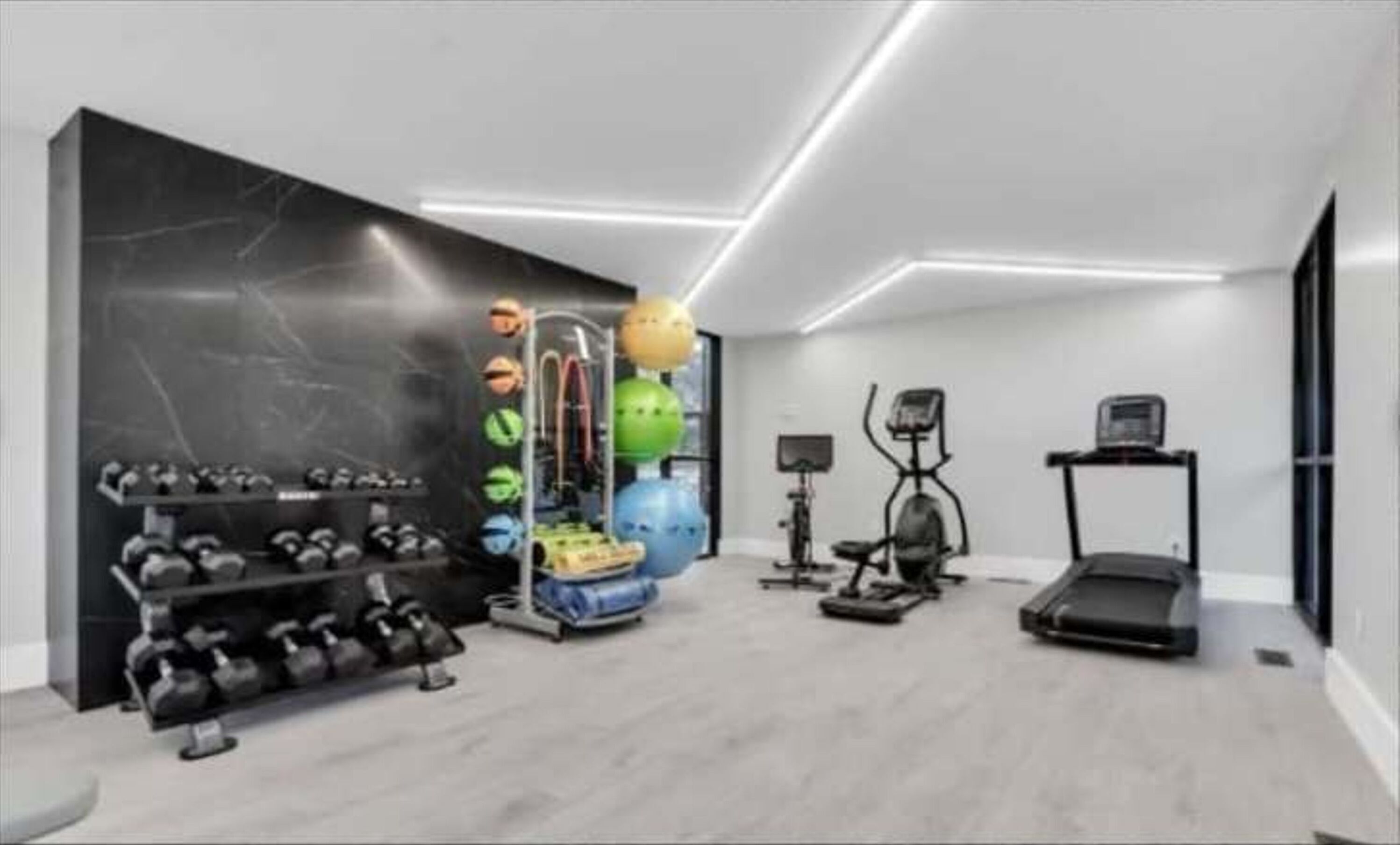 A modern gym with exercise equipment, a treadmill, and a wall-mounted rack of dumbbells.
