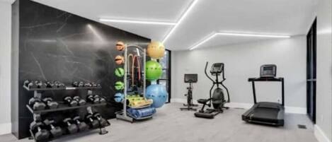 A modern gym with exercise equipment, a treadmill, and a wall-mounted rack of dumbbells.