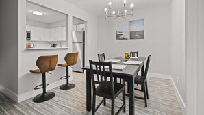 A modern kitchen with white cabinets, a built-in microwave, and a refrigerator. There is a dining area with a black table and chairs, and a chandelier above. - Tranquil 2BR 2BA Getaway for the Family (Rochester)