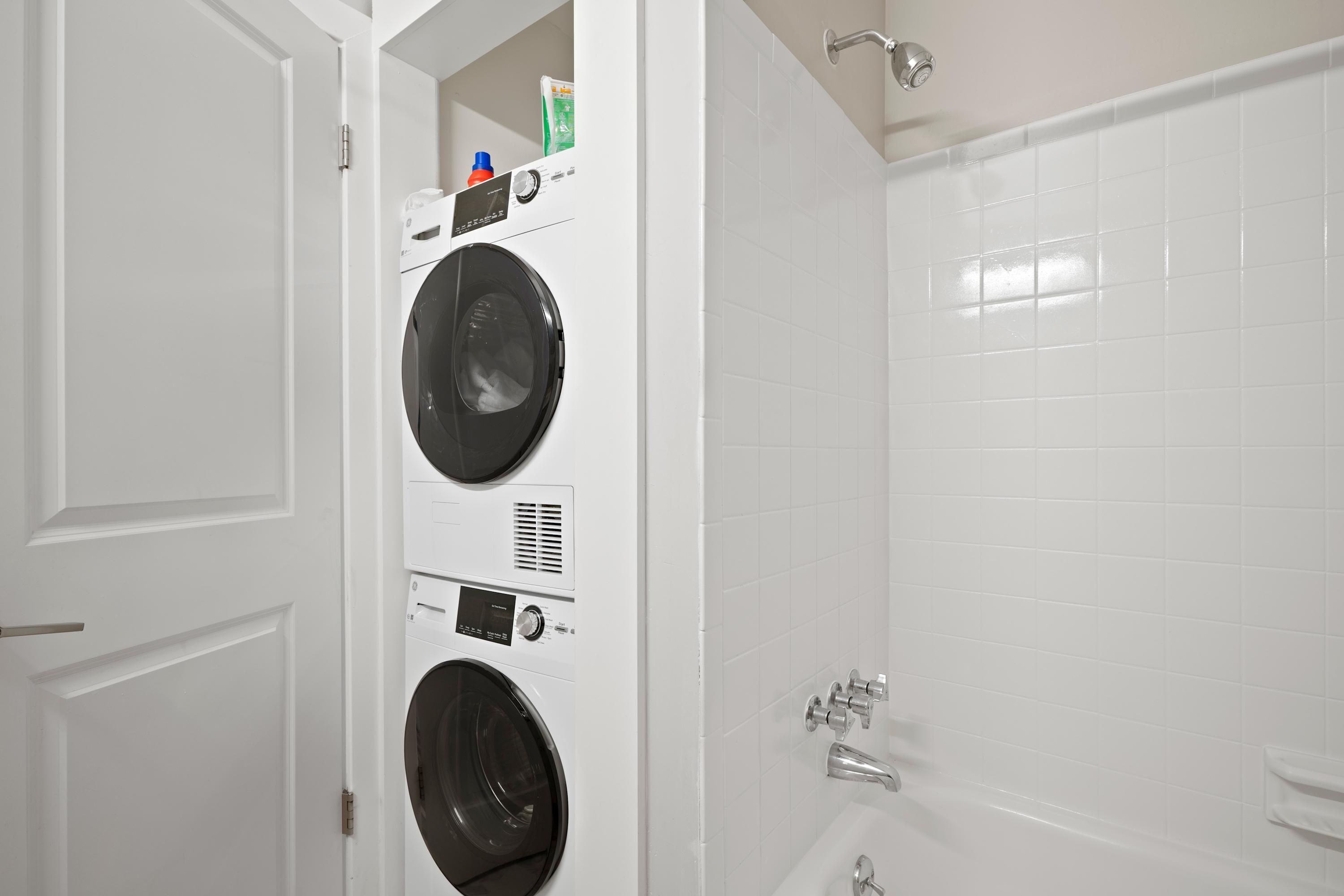 A laundry room with stacked washing machines and a bathtub.