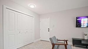 A room with a wooden chair, a TV mounted on the wall, and a door. - Comfortable 2BR 2BA Home Away From Home (Rochester)