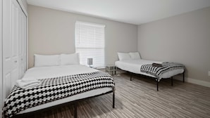 A bedroom with two beds, a white wardrobe, a bedside table, and a window with blinds. - Comfortable 2BR 2BA Home Away From Home (Rochester)