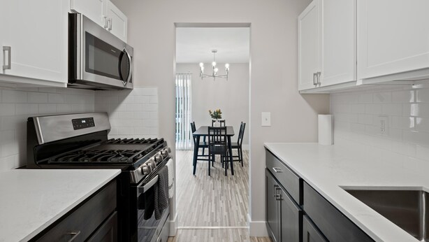 A modern kitchen with white cabinets, stainless steel appliances, and a dining area with a chandelier. - Comfortable 2BR 2BA Home Away From Home (Rochester)