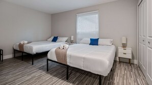 A hotel room with two beds, a window with blinds, a bedside table with a lamp, and a wardrobe. - Spacious 2BR 1BA Haven - Perfect for Families (Rochester)
