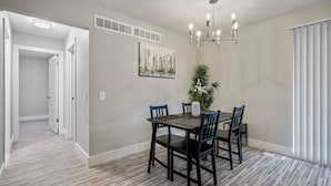 A dining area with a dark wooden table and chairs, a chandelier, a painting on the wall, and a plant. - Spacious 2BR 1BA Haven - Perfect for Families (Rochester)