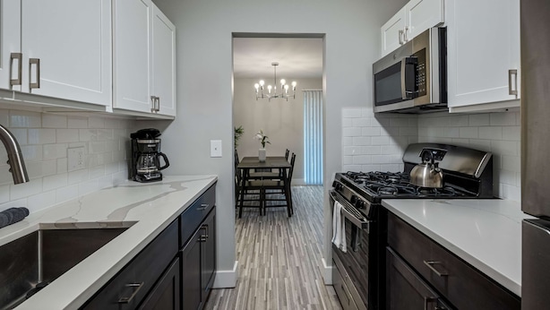 A modern kitchen with white cabinetry, a stainless steel sink, a coffee maker, a stove, and a microwave. - Spacious 2BR 1BA Haven - Perfect for Families (Rochester)