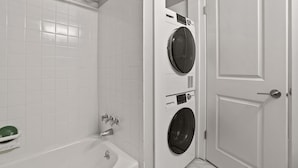 A modern bathroom with a white tiled wall, a built-in washing machine, a bathtub, and a door. - Spacious 2BR 1BA Haven - Perfect for Families (Rochester)