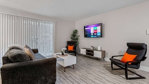 A modern living room with a sofa, a black and orange chair, a coffee table, and a TV mounted on the wall. - Spacious 2BR 1BA Haven - Perfect for Families (Rochester)