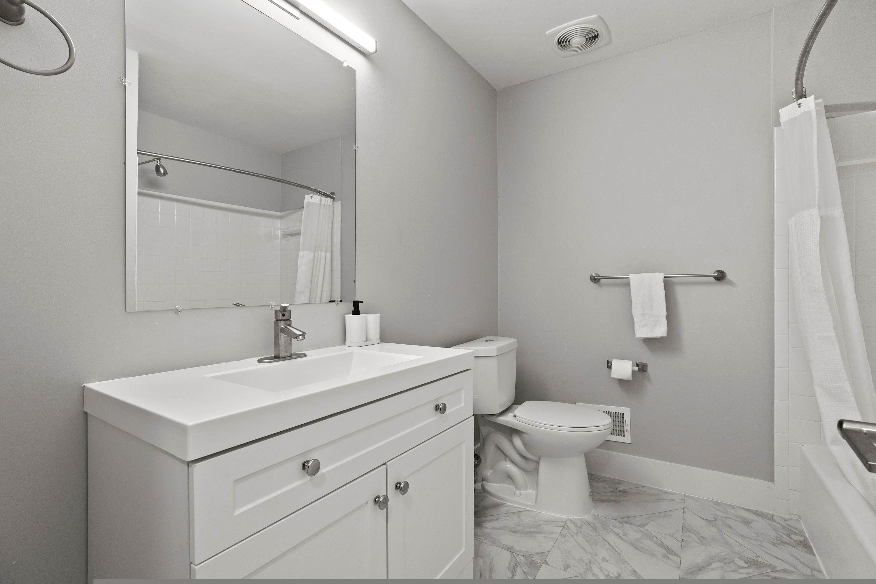 A modern bathroom with a white vanity, a toilet, and a shower area.